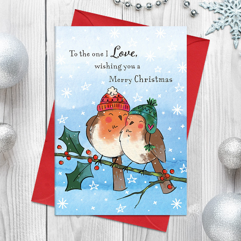 To the One I Love Christmas card featuring two illustrated robins nestled together in winter hats on a holly branch, surrounded by snowflakes and stars.