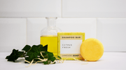 Laneside Soap Co Citrus Fresh Shampoo Bar 60g with its yellow box styled on a bathroom shelf with green foliage and a glass bottle of oil