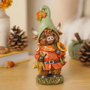 Highland cow autumn figurine lifestyle shot on wooden surface surrounded by pine cones and autumn pumpkin display