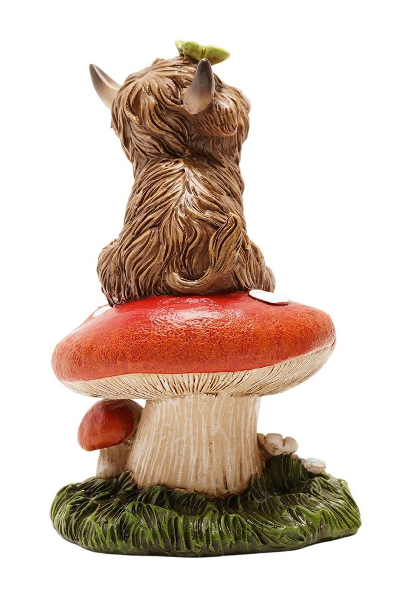 Highland Cow Sitting on Toadstool Figurine back view showing shaggy fur detail, curved horns and butterfly on head, seated on spotted toadstool, on white background