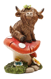 Highland Cow Sitting on Toadstool Figurine side view showing highland cow with curved horns and butterfly seated on spotted toadstool with wildflowers at base, on white background