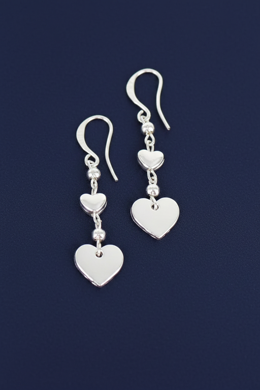 Silver plated drop earrings with two graduating heart charms linked by silver plated beads on hook fittings, on a deep navy blue background