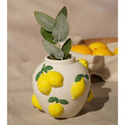 Hestia white ceramic vase with lemon design 12cm, next to a bowl of lemons with green leaves arranged inside the vase 