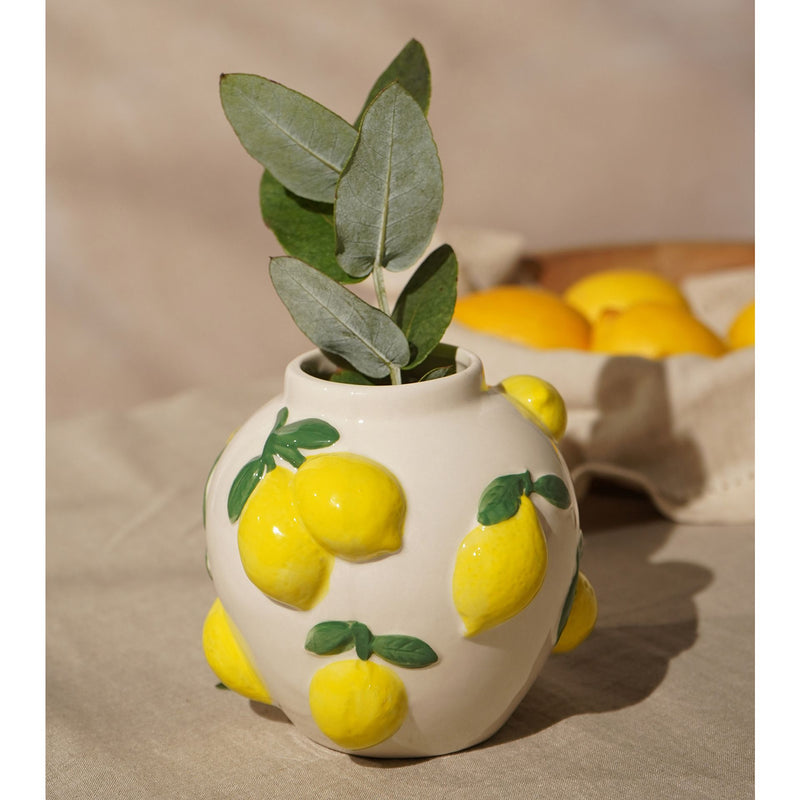 Hestia white ceramic vase with lemon design 12cm, next to a bowl of lemons with green leaves arranged inside the vase 