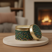 Belly Button Designs Warm Winter soy wax candle in dark green and gold tin on a beige board with lit fireplace in background