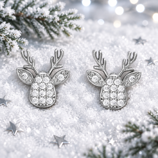 Pair of rhodium plated Cubic Zirconia reindeer head earrings lying flush in soft snow, surrounded by silver star confetti and frosted evergreen sprigs with cool bokeh fairy lights in the background