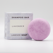 Laneside Soap Co Lavender Shampoo Bar 60g in a round disc shape alongside its lilac botanical gift box, on a light grey background