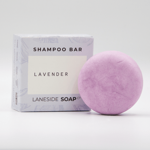 Laneside Soap Co Lavender Shampoo Bar 60g in a round disc shape alongside its lilac botanical gift box, on a light grey background