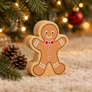 Wooden gingerbread man toy beneath Christmas tree branches beside small pinecones and warm fairy lights