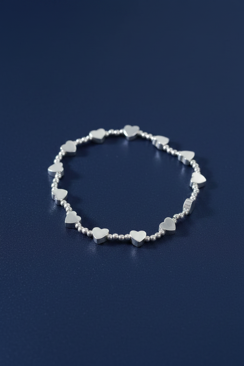 Silver plated elasticated bracelet with thirteen heart charms and round silver beads, laid flat in a circle on a deep navy blue background