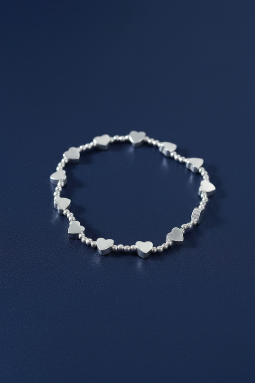 Silver plated elasticated bracelet with thirteen heart charms and round silver beads, laid flat in a circle on a deep navy blue background