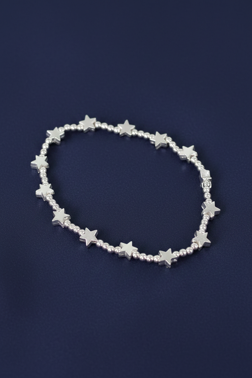 Silver plated elasticated bracelet with silver star charms and round beads, laid flat in a circle on a deep navy blue background