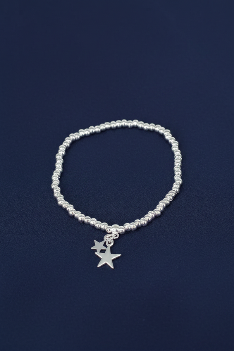 Silver plated elasticated bracelet with two dangling silver star charms on a ball bead band, on a deep navy blue background