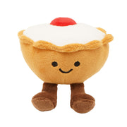 Front view of a soft plush Bakewell tart toy with a golden pastry case, smooth white icing top, fluffy red cherry, smiling face and fluffy brown legs and feet, on a white background