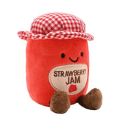 Angled view of a soft red plush strawberry jam jar toy with a stitched Strawberry Jam label, smiling face, red and white gingham hat and fluffy brown feet, on a white background