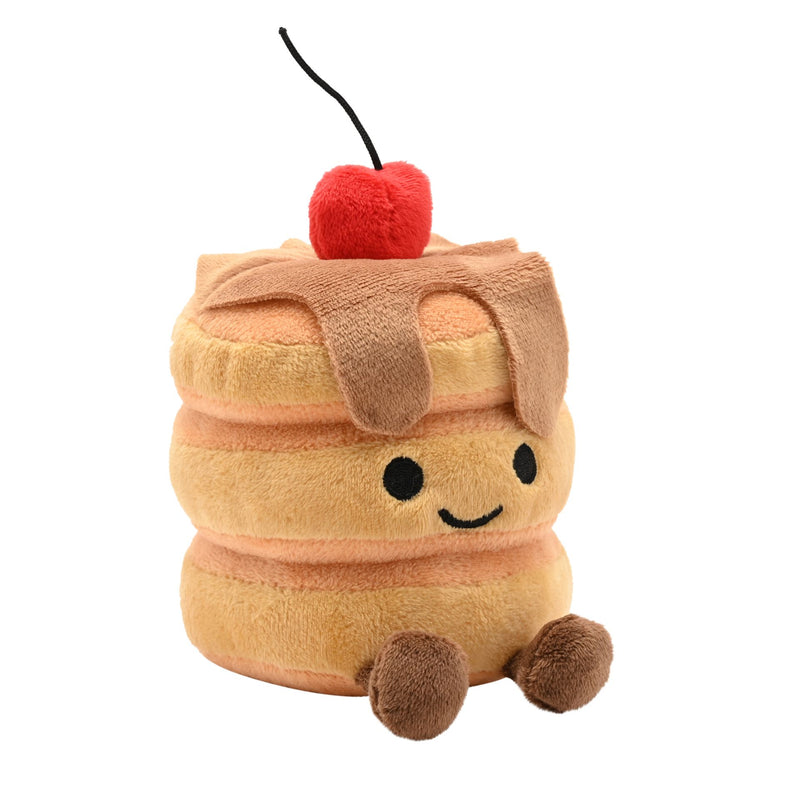 Angled front view of a soft plush pancake stack toy with three golden pancakes, syrup drizzle, a smiling face, fluffy red cherry on top and fluffy brown feet, on a white background