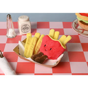 A red plush French fries carton toy with removable yellow fry pieces, sitting in a paper food tray on a pink and white checked tablecloth with salt and pepper shakers in the background