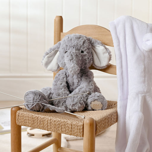 Ethel the Elephant plush soft toy sitting on a wooden chair with knitting needles and yarn