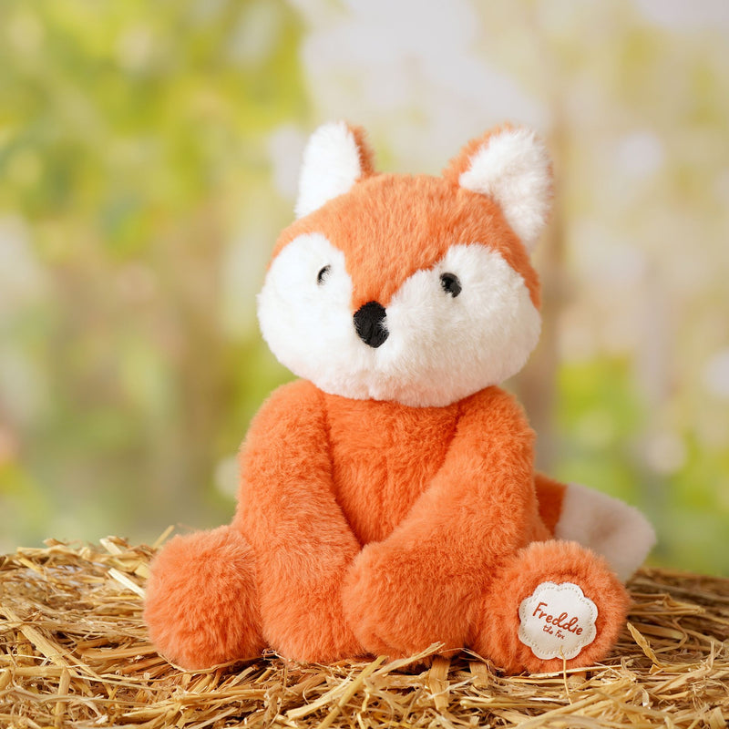 Freddie the plush sitting fox soft toy 22cm, lifestyle shot sitting on a bed of straw— a cuddly companion for fox lovers and little adventurers