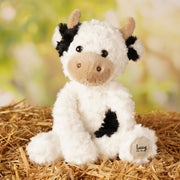 Lucy the plush cow soft toy 23cm, lifestyle shot — sitting on a bed of  straw