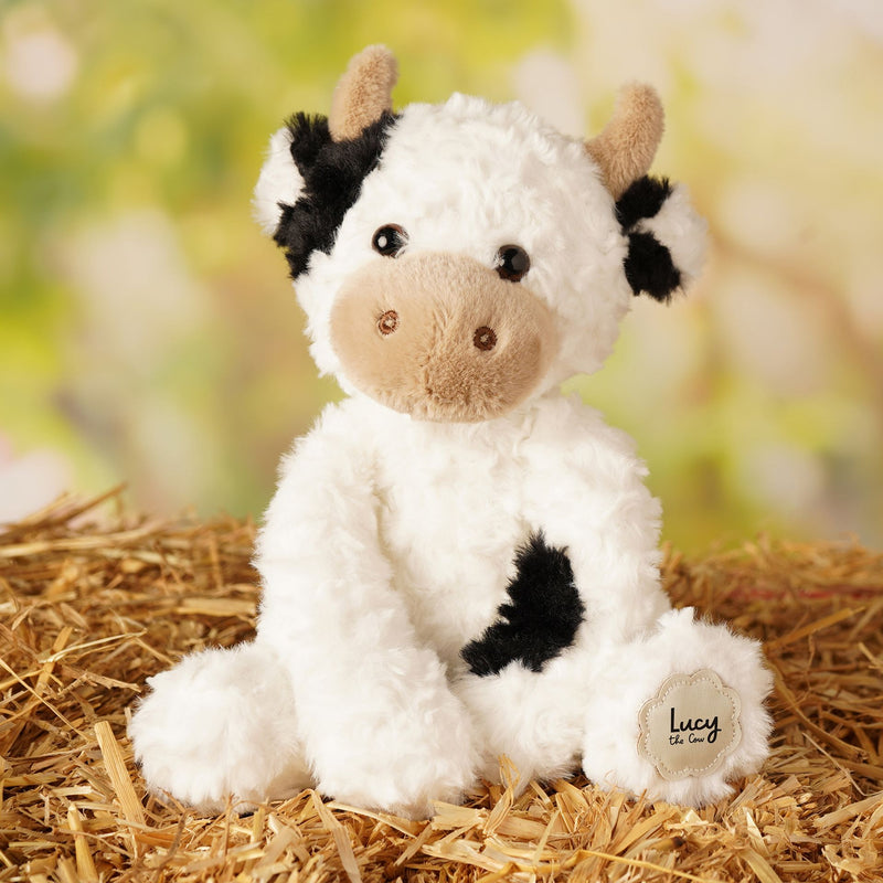 Lucy the plush cow soft toy 23cm, lifestyle shot — sitting on a bed of  straw