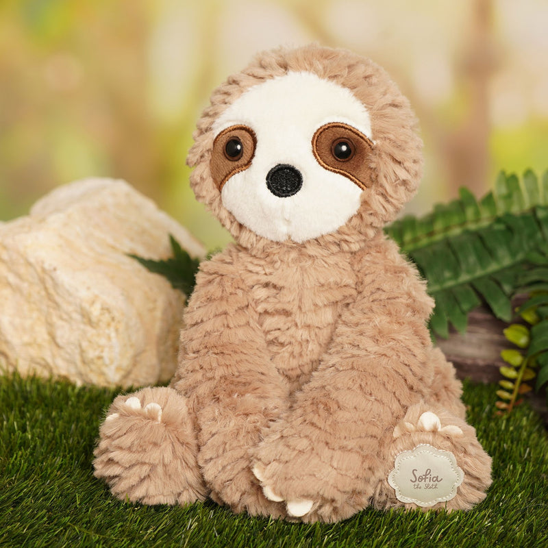 Sofia plush sitting sloth nestled in a forest setting, lifestyle shot among green leaves 