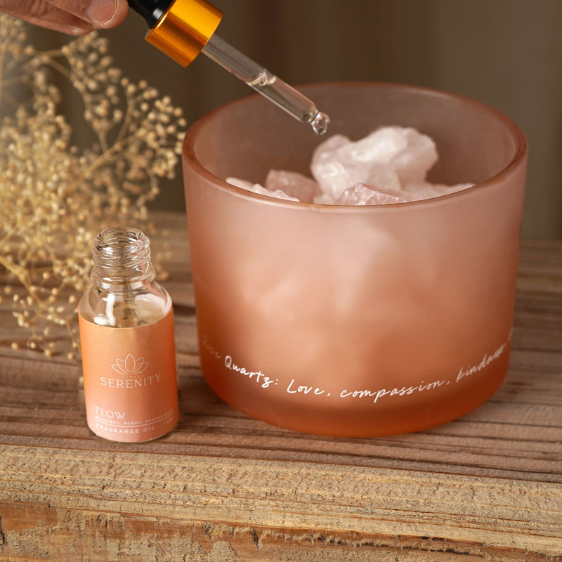 Hand adding fragrance oil with dropper into rose quartz crystal bowl diffuser on wooden surface with dried flowers