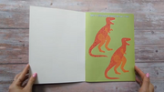 Inside page of Dinosaur Sticker Book showing spot the difference activity with two orange T-rex illustrations on a green background