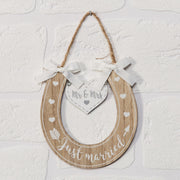 Just Married Wooden Horseshoe Hanging Plaque displayed on white brick wall showing natural wood finish with Just Married script and Mr and Mrs heart tag
