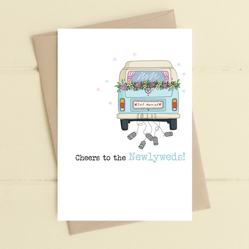 Wedding card featuring an illustrated vintage campervan decorated with a floral garland just above the rear window and a Just Married numberplate with tin cans trailing behind and the sentiment Cheers to the Newlyweds